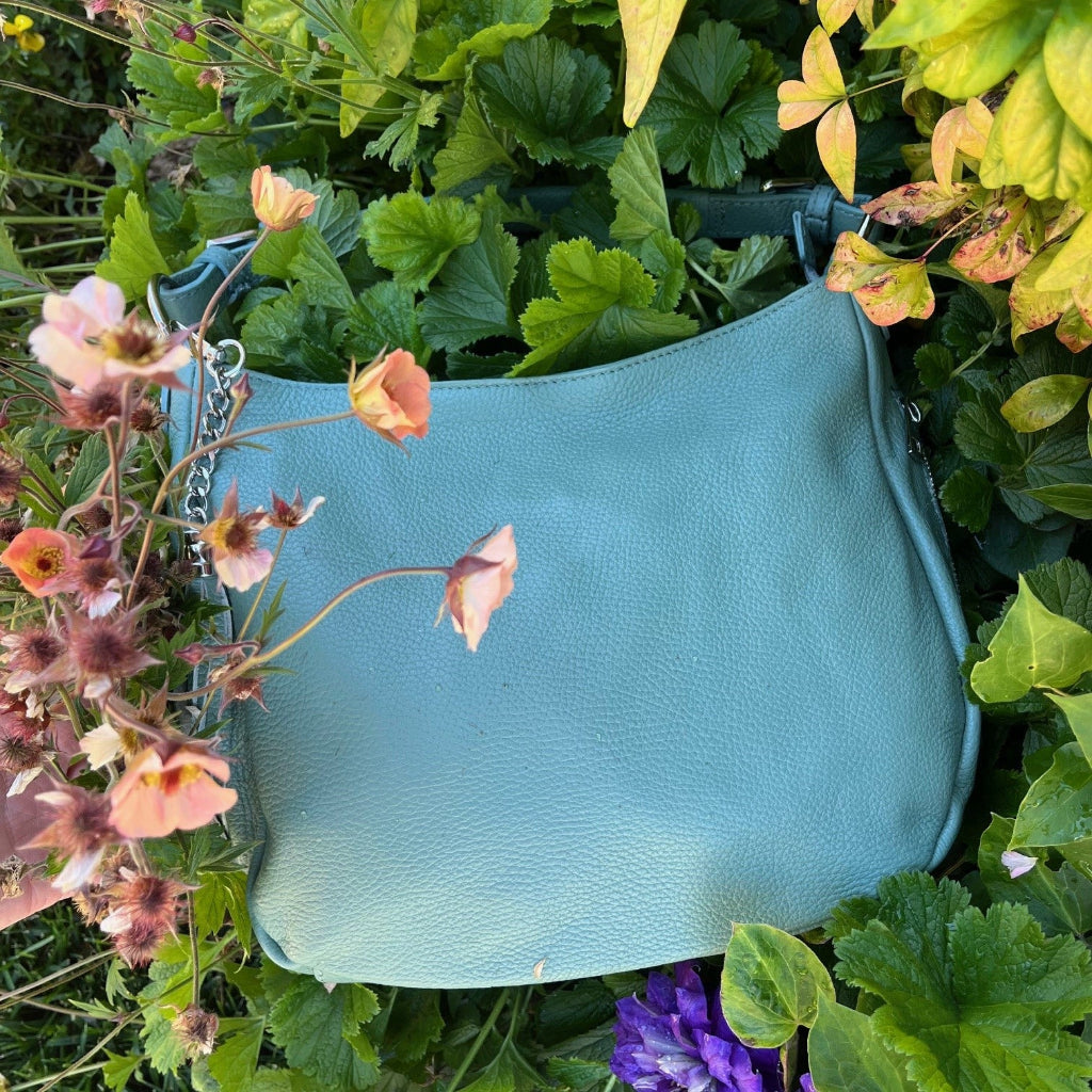 Sage green handbag among green foliage and flowers