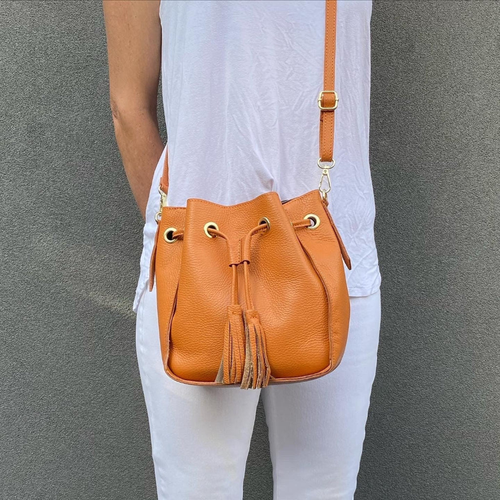 Person holding a tan leather bucket bag 