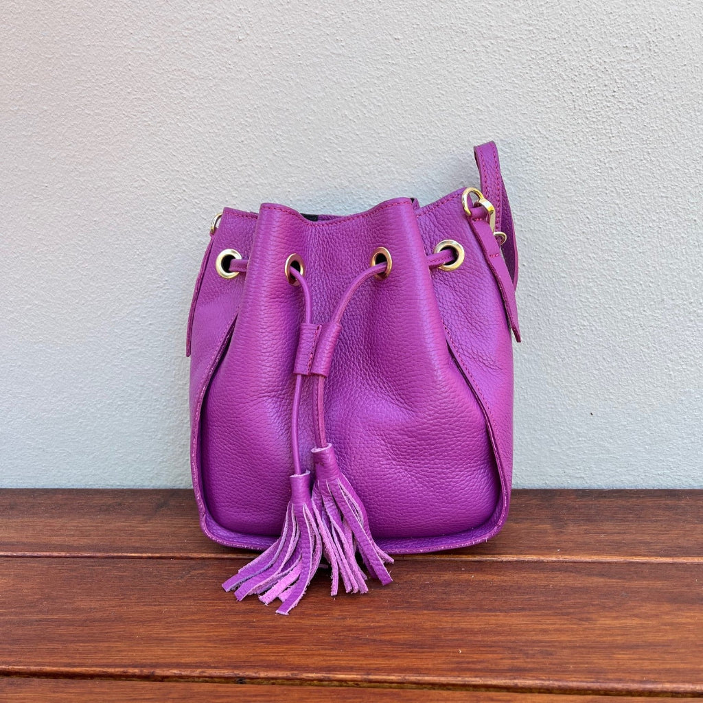 Pink leather bucket bag with a tassel on a wooden surface 