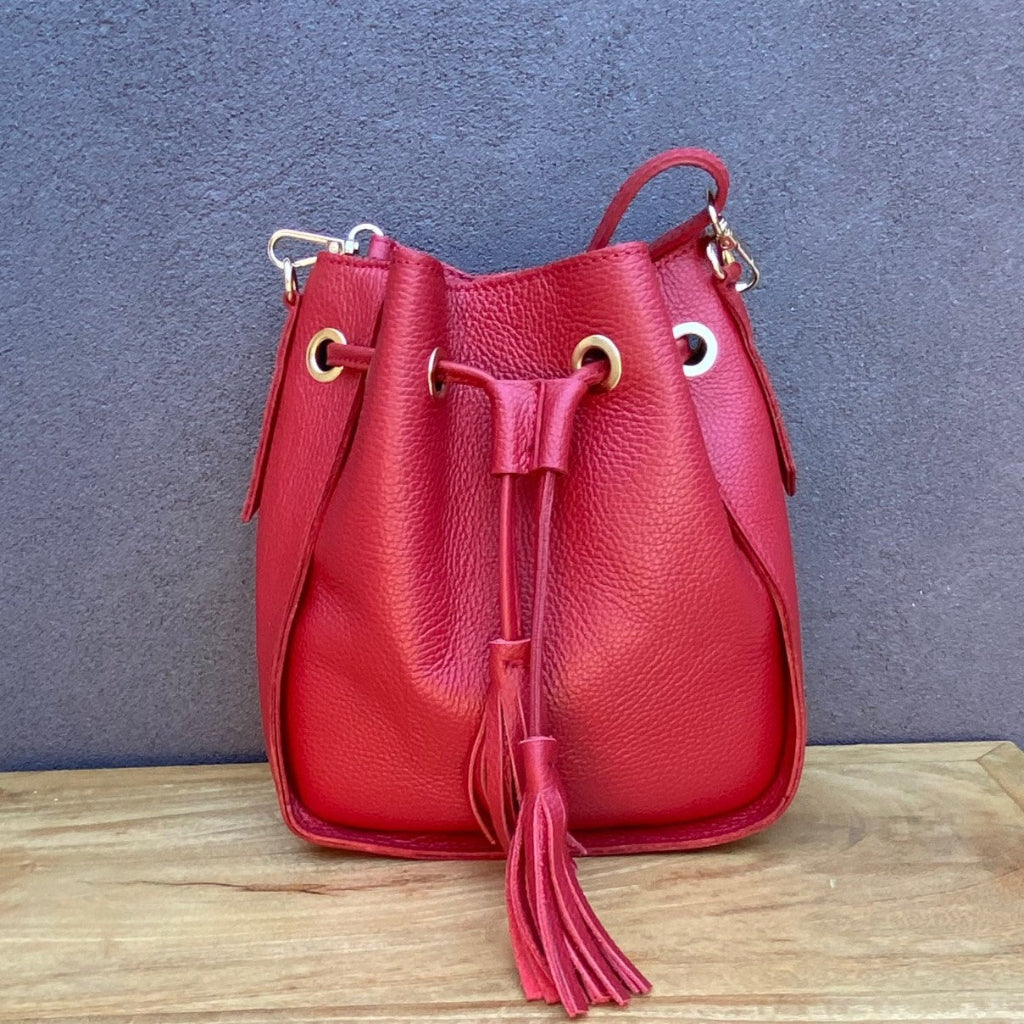 Red leather bucket bag with a tassel on a wooden surface 