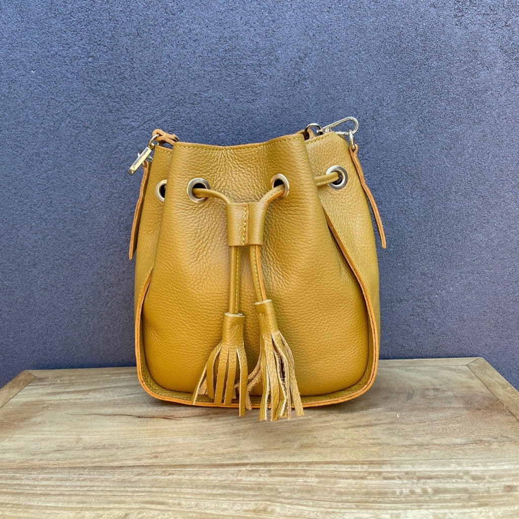Yellow leather bucket bag with tassels on a wooden surface 