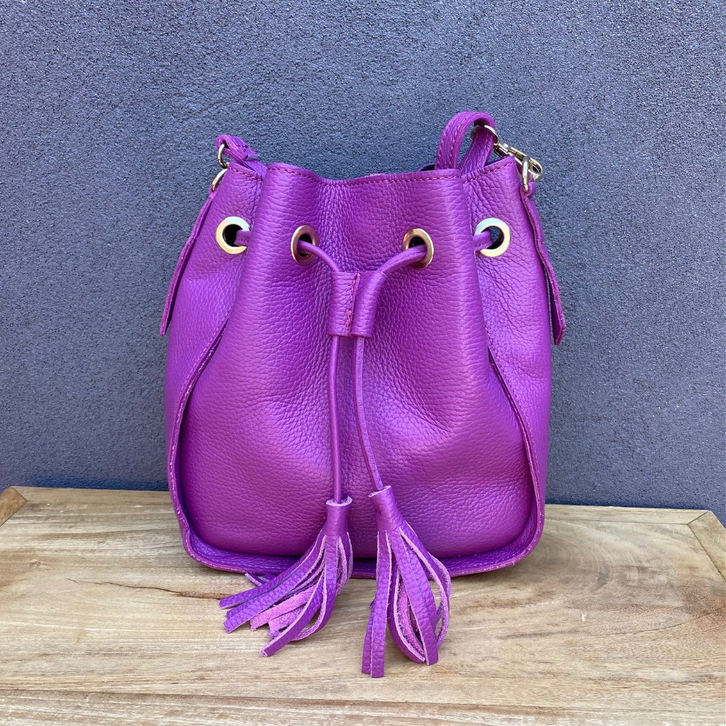Purple leather bucket bag with tassels on a wooden surface and blue background