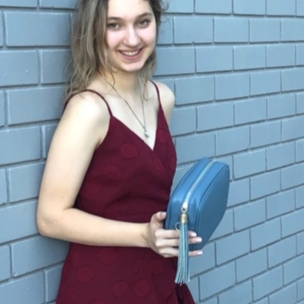 Woman against a wall holding the Ella cross body bag in denim blue